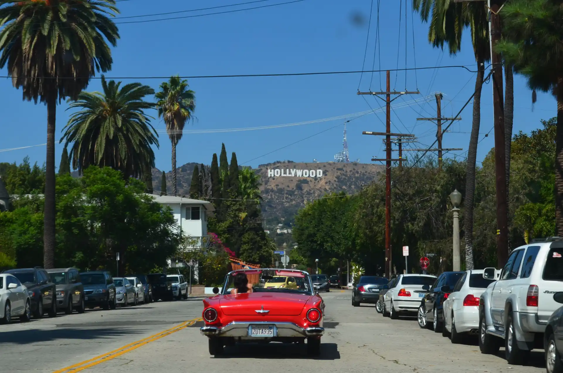 Carro em rua de Los Angeles com letreiro de Hollywood ao fundo